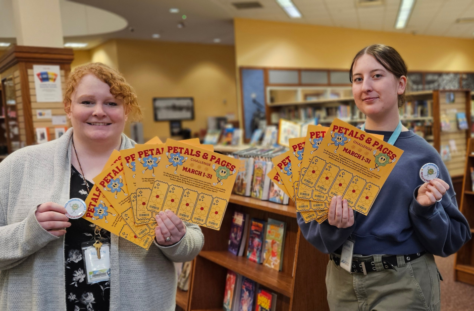 two library staff holding up petals and pages ticket boards