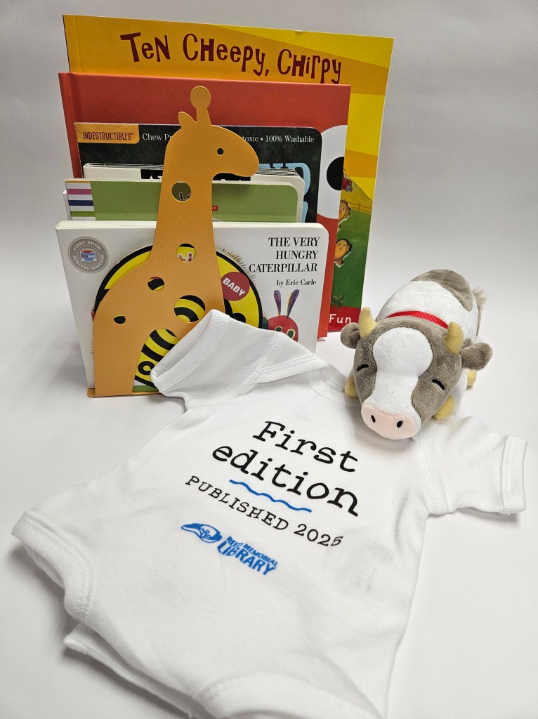 Some children's books, a stuffed cow, and a baby onesie with "first edition, published 2025" printed on it.