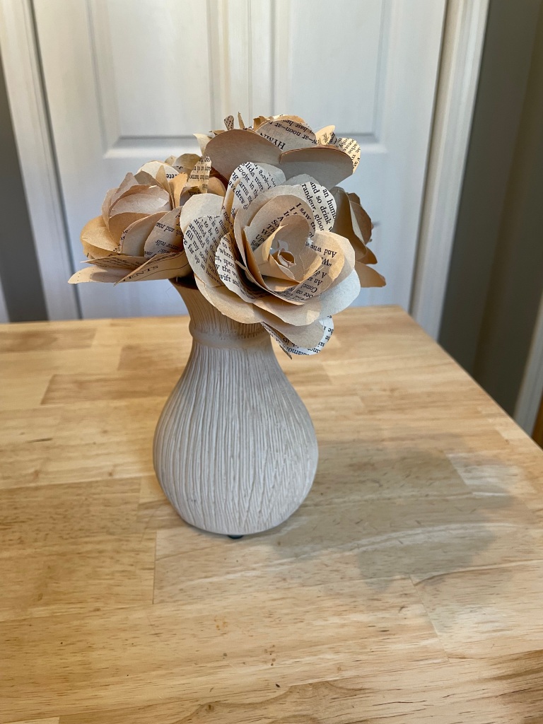 white vase holding a bouquet of book page roses
