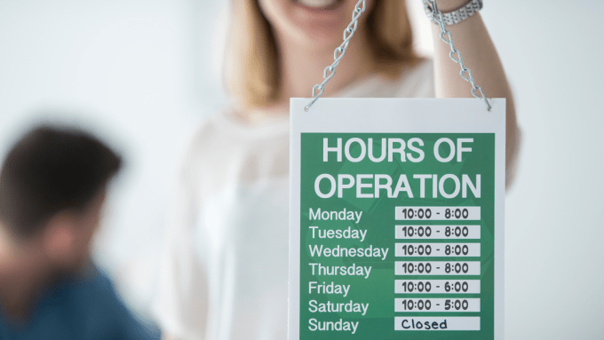 person holding a business hours sign showing the days of week and hours open each day.