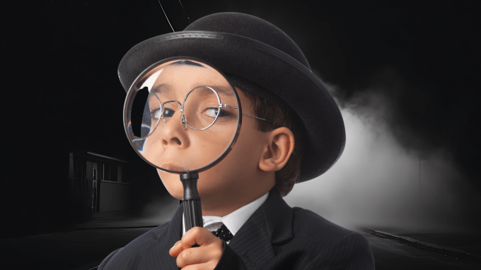 boy in a bowler hat looking ahead closely through a magnifying glass