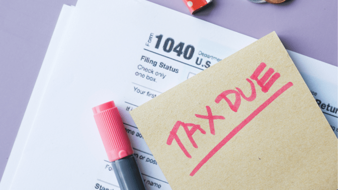 tax forms laying on a desk, with office accessories nearby and a note reading, "tax due" on top